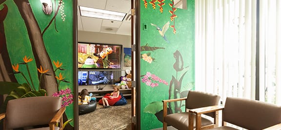 Two children sitting in bean bag chairs enjoying the games and TVs in the waiting area